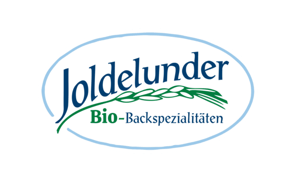 Logo von „Joldelunder Bio-Backspezialitäten“ in ovaler Form: dunkelblauer Schriftzug „Joldelunder“, darunter grün-blau „Bio-Backspezialitäten“, links davon stilisierte grüne Ähre, eingefaßt von einem hellblauen Ovalsrahmen.